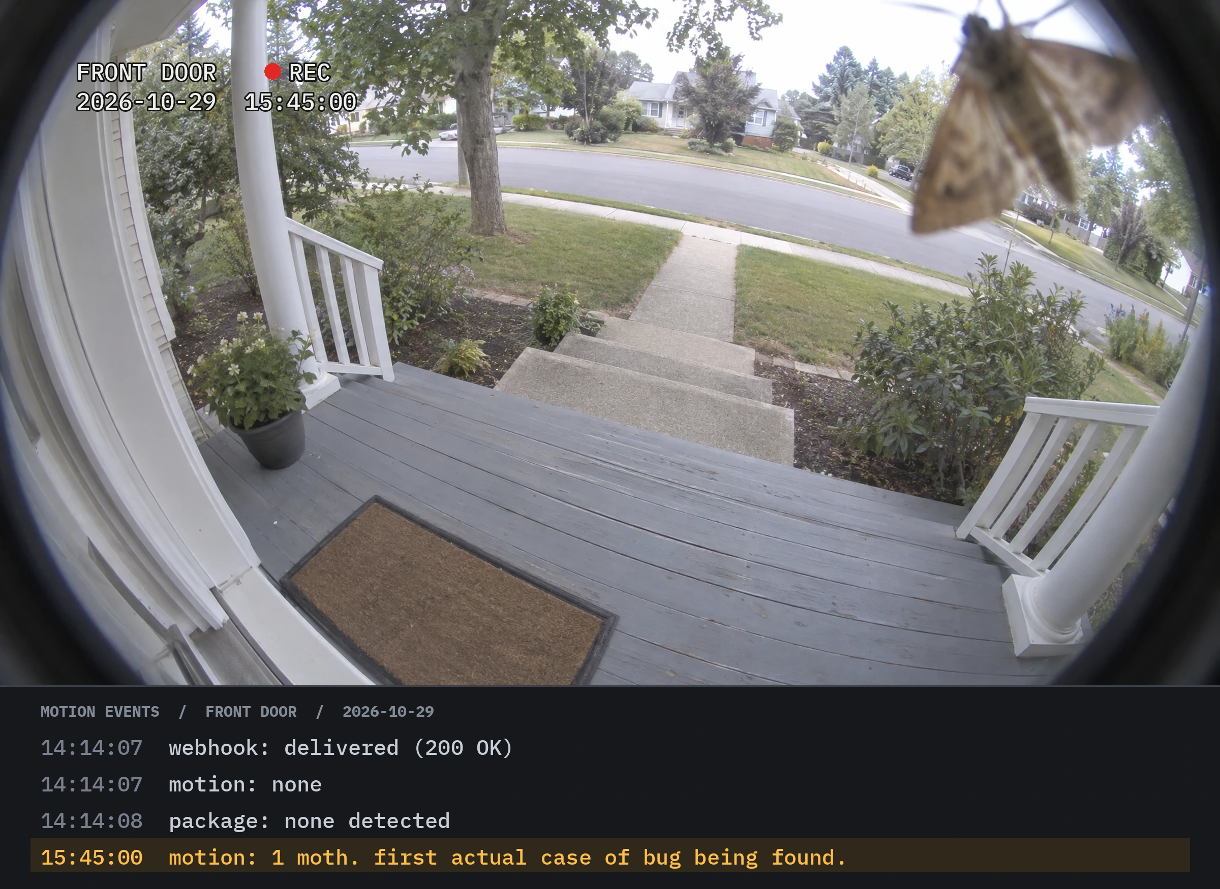 A fisheye doorbell camera still of an empty front porch with a doormat, white railings, a potted plant and a quiet suburban street. A large moth sits on the lens in the top right. On-screen text: FRONT DOOR, red REC dot, 2026-10-29 15:45:00. Below, a dark app panel titled MOTION EVENTS / FRONT DOOR / 2026-10-29 lists: 14:14:07 webhook: delivered (200 OK). 14:14:07 motion: none. 14:14:08 package: none detected. The last row is highlighted in amber: 15:45:00 motion: 1 moth. first actual case of bug being found.